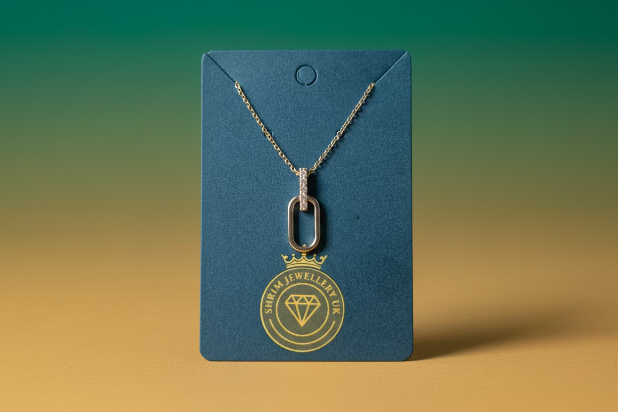 Silver necklace with a pendant on a blue card with a brand logo, placed on a beige surface.